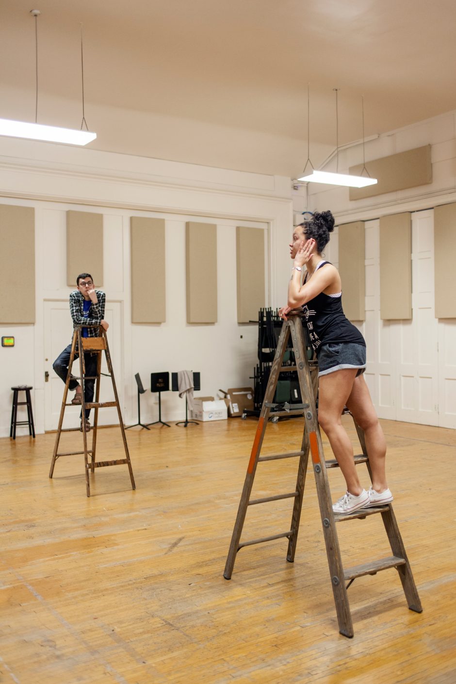 Students standing on ladders in a rehearsal studio.