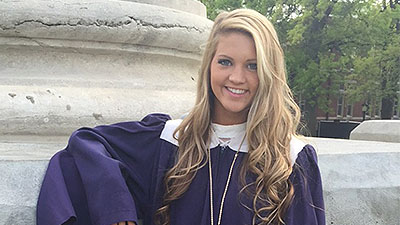 Libby Martin in a graduation cap and gown leaning against one of the Columns.