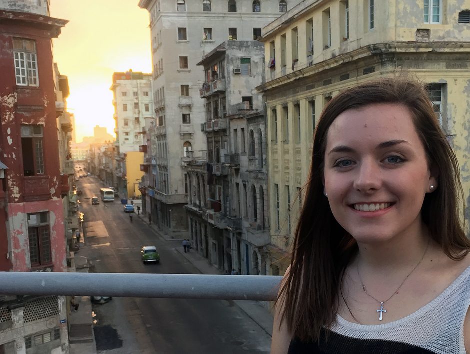 Lauren Alexander stands on a balcony overlooking a sunset on a bustling city street.
