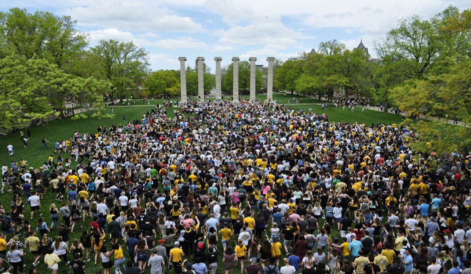 Thousands of students walk toward the columns on their way into the world.