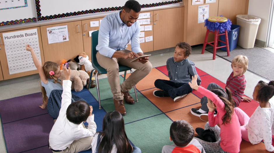 A teacher uses an iPad to teach a group of kindergarteners.