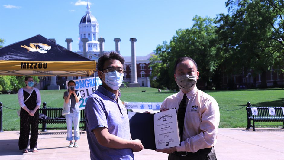 man handing another man a certificate in front of jesse hall