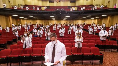 students in white coats, socially distanced, reading