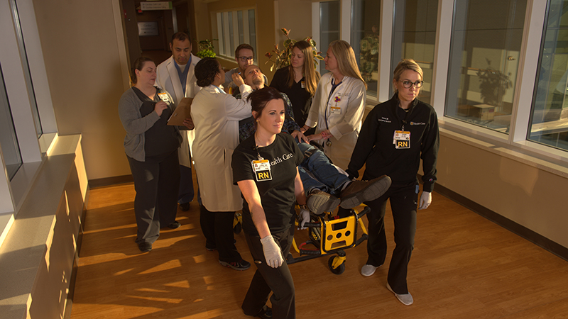a group of health care professionals wheeling a patient on a medical gurney through a hospital