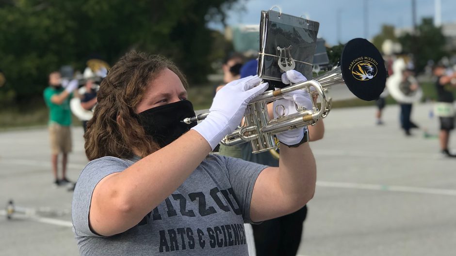 Catherine Hutinett plays the trumpet with a black face mask on