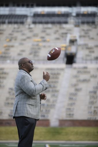 chatman on a football field tossing a ball up, in a grey suit and dark pants