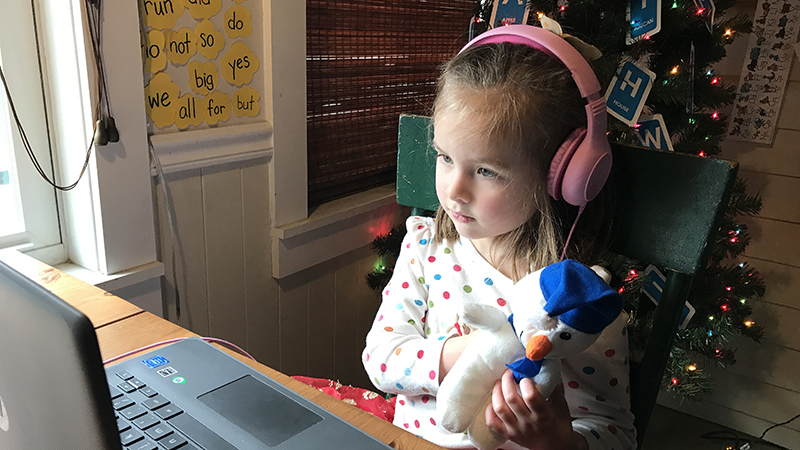 a little girl at a computer with headphones on