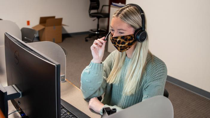 woman with a face covering on the phone at her computer