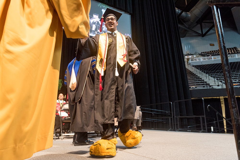 a student with Truman's costume feet crosses the stage at commencement to receive his diploma