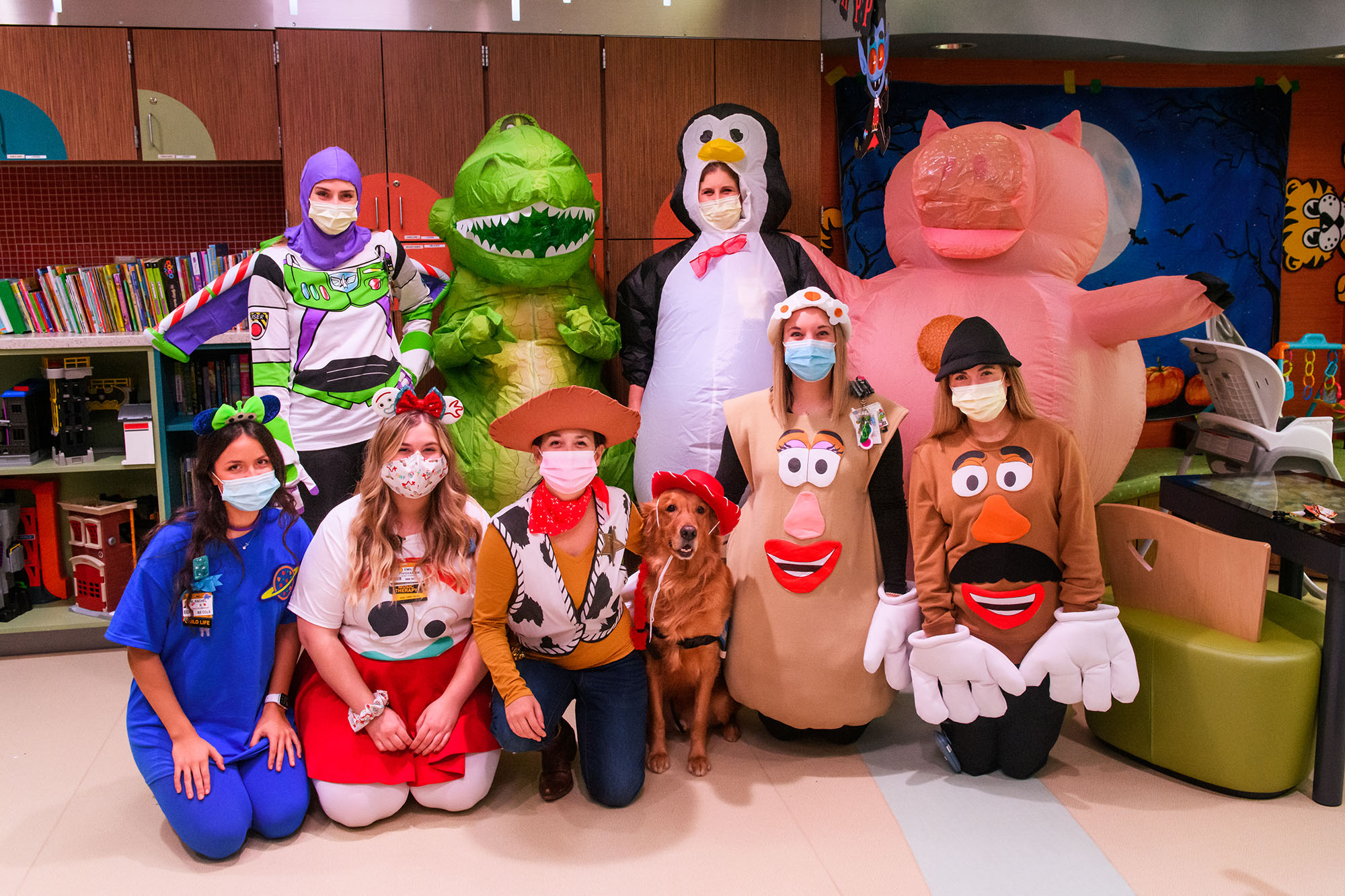 a group photo of employees dressed as toy story characters. the therapy dog is in the center, dressed as jessie