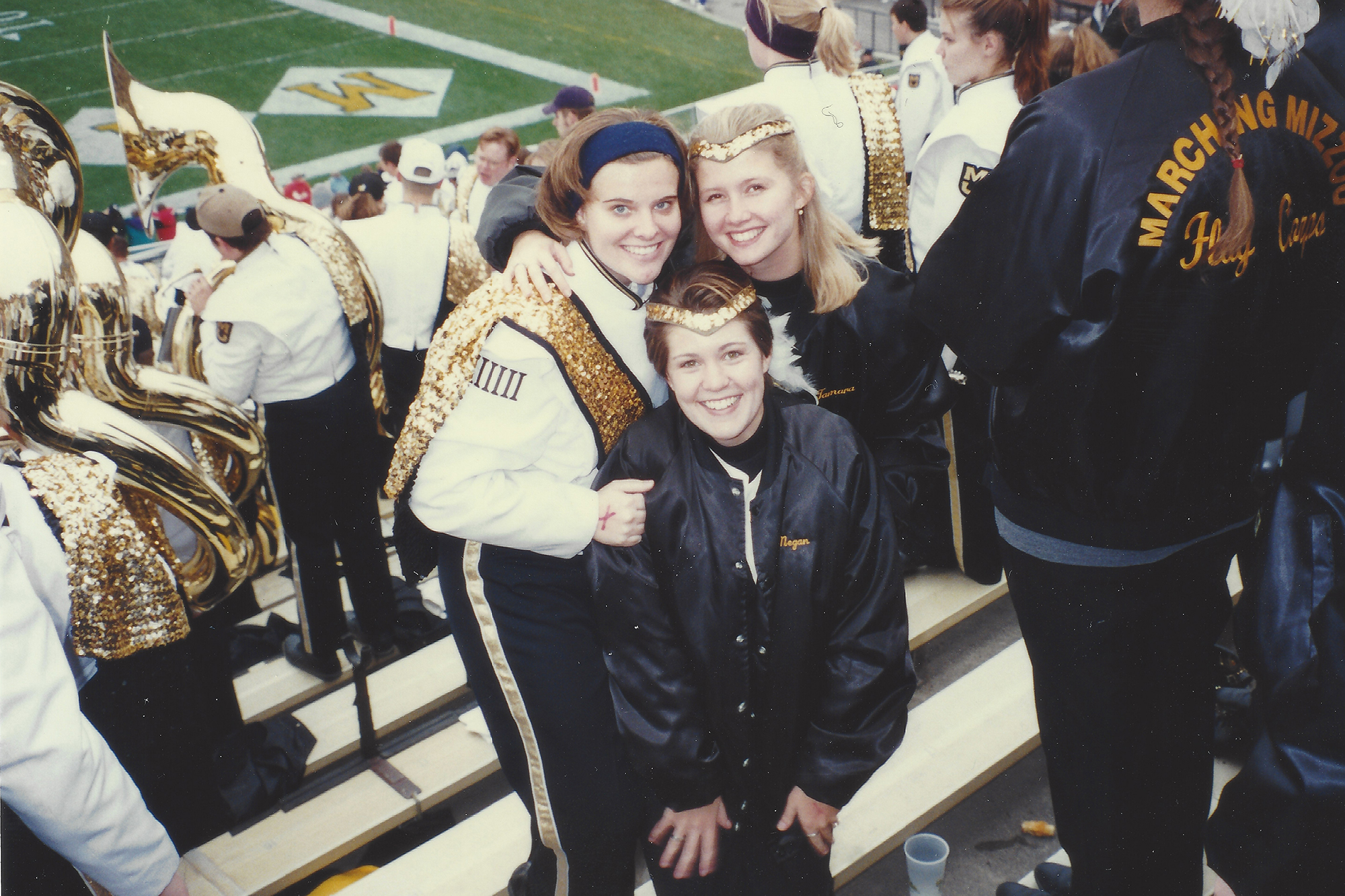 three young women pose for a photo. you can see they're part of marching mizzou and are at a football game