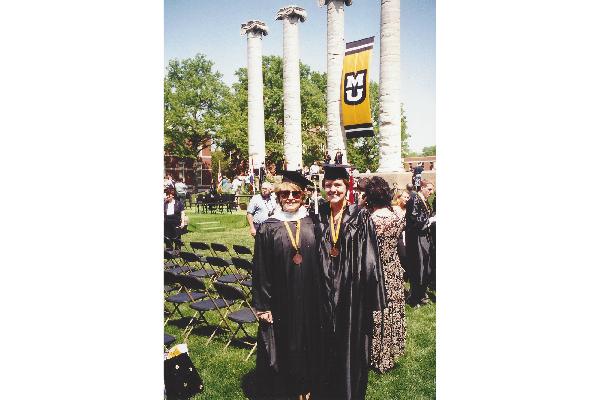Megan Silvey and Suzette Heiman pose for a photo during an outdoor graduation ceremony in front of the columns