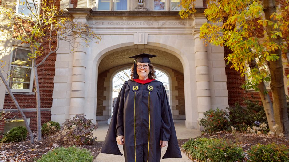 Megan Silvey stands in her regalia in front of the J-School archway