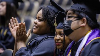 photo of three students at commencement. they're smiling and clapping during the ceremony
