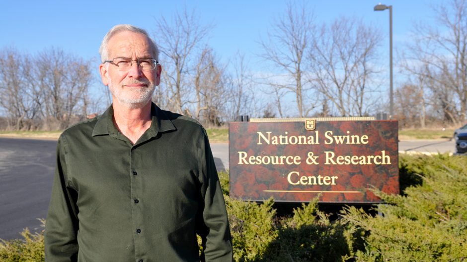 A photo of Dr. Randall Prather standing in front of a sign for the National Swine Resource & Research Center.