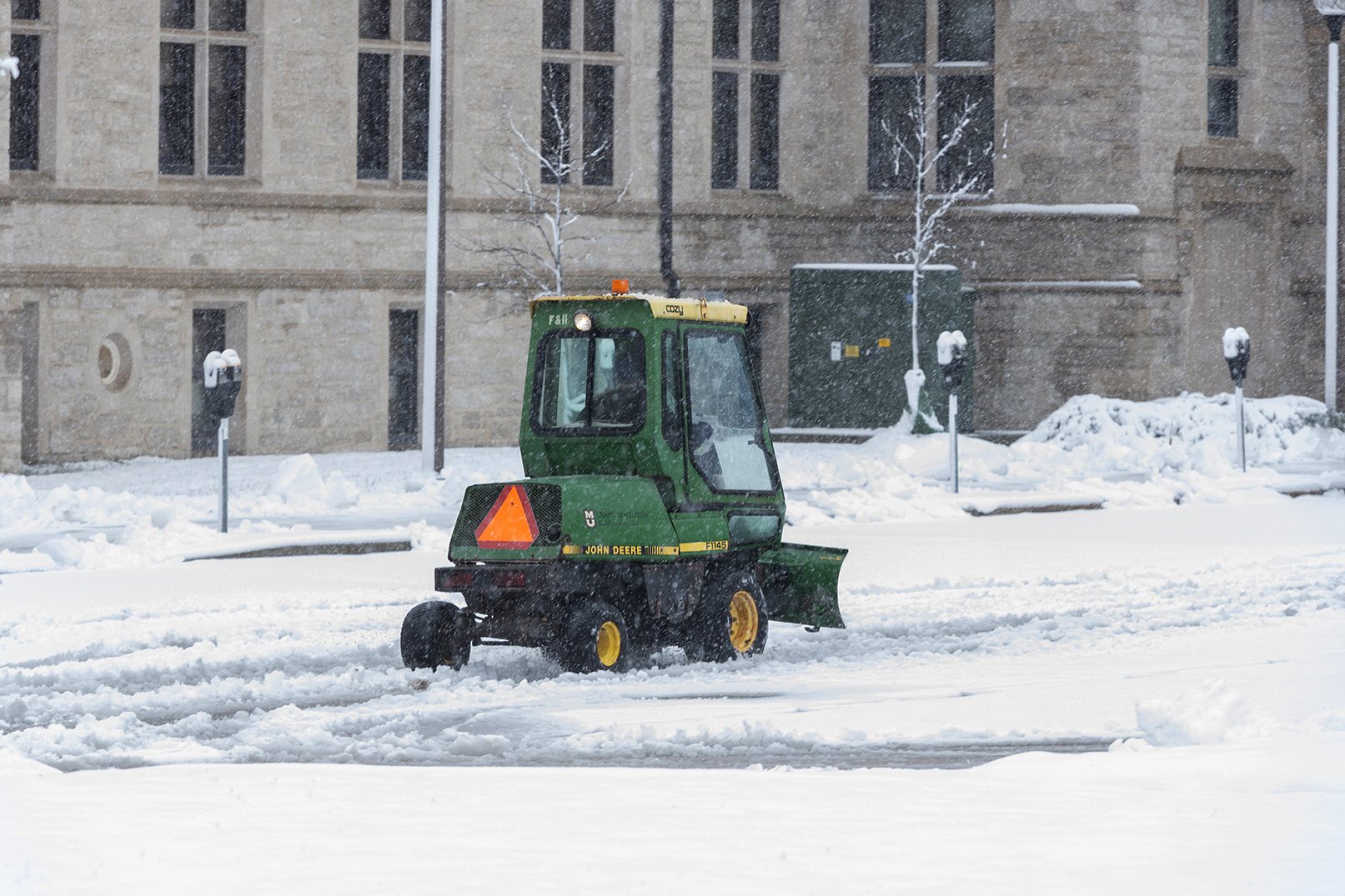 a landscape services vehicle helps clear snow from a sidewalk
