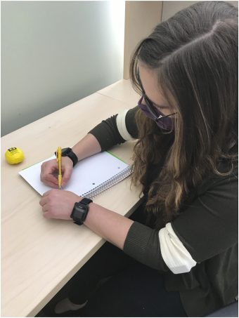 Person sitting at a desk writing on a sheet of paper with sensors attached on both arms