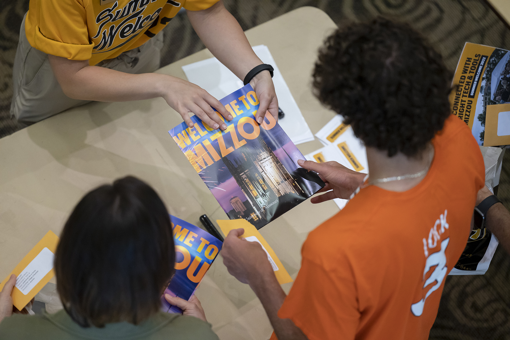 a student hands a new student a "welcome to mizzou" book