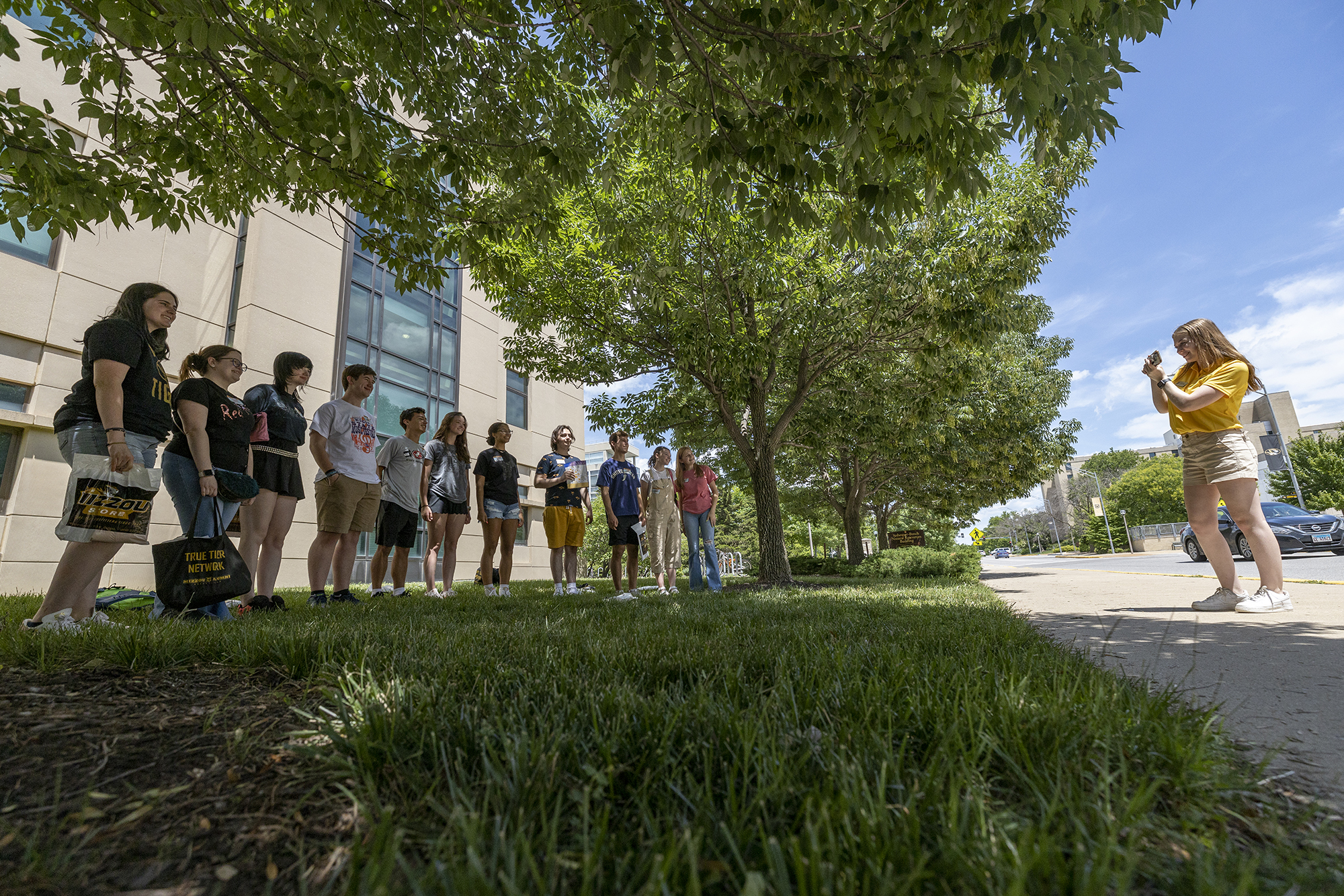 a wide shot of a summer welcome leader taking photos of a group of new students