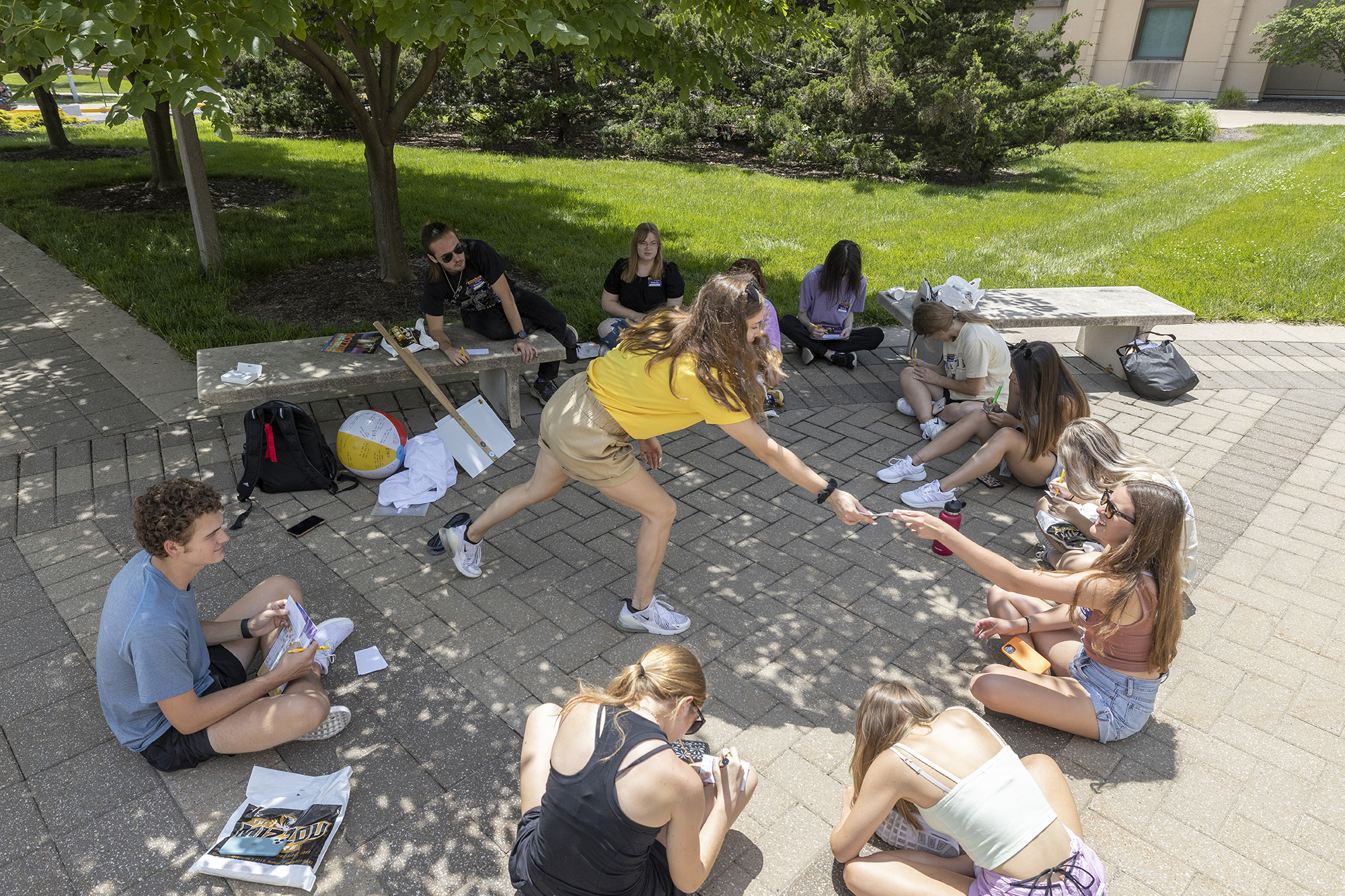 a group of new students sit in a circle and work on an activity in the shade outside