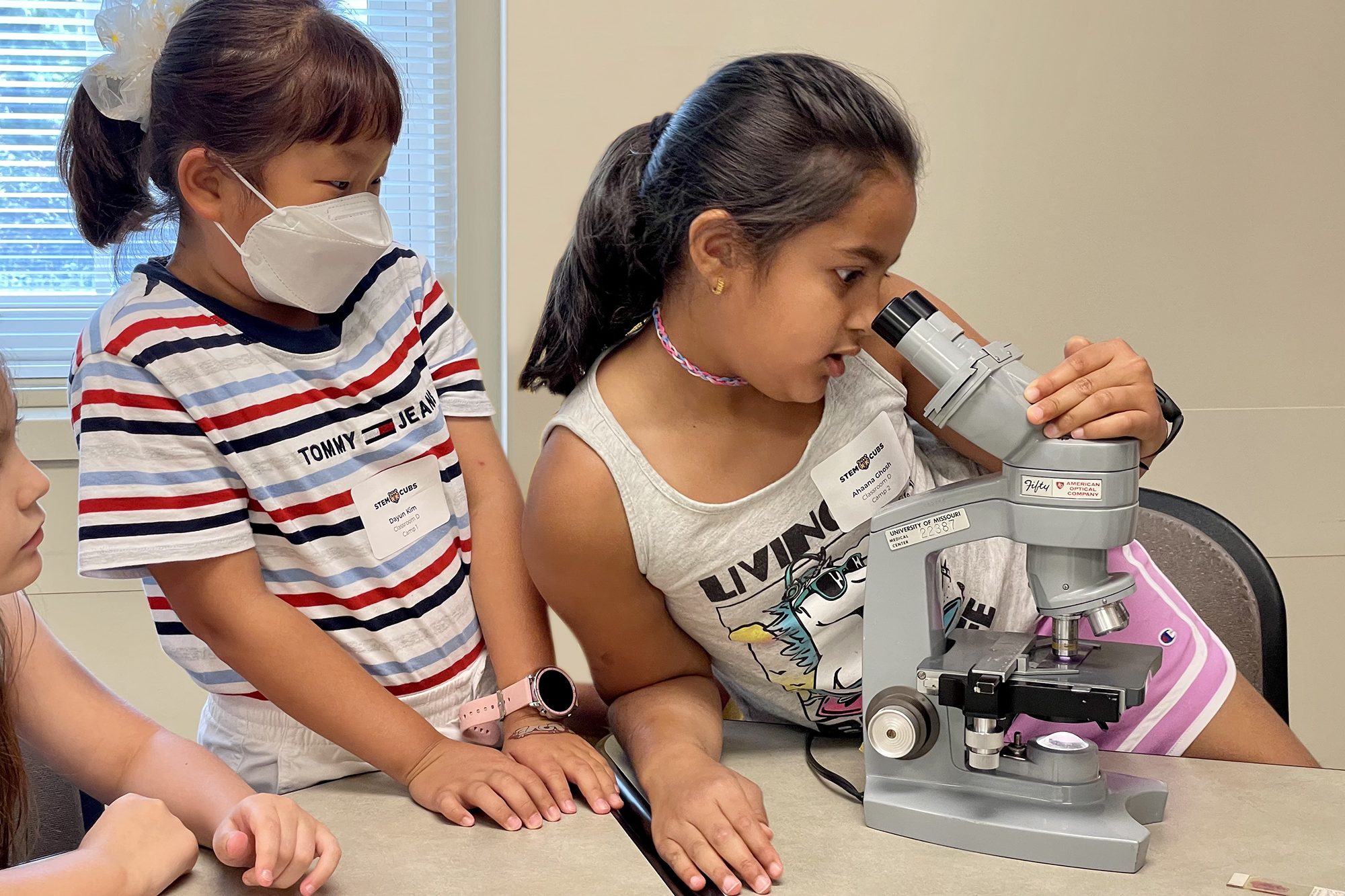 two young girls look at a microscope