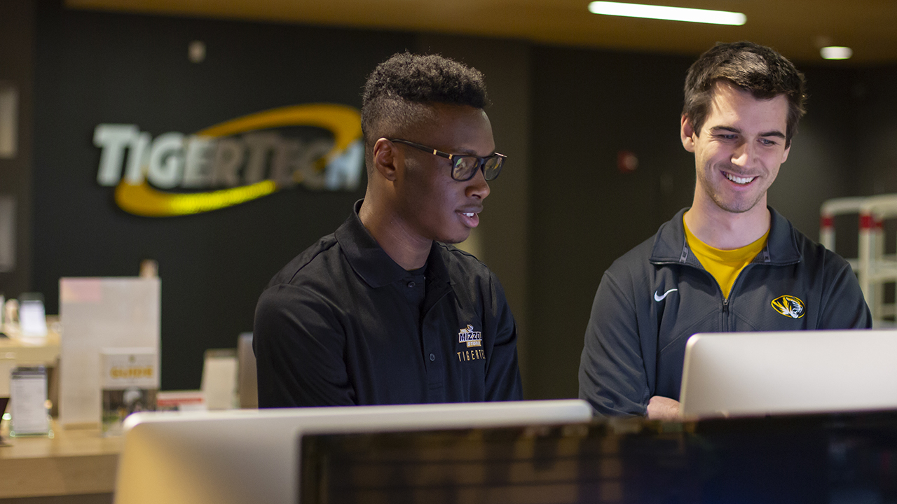 two young men look at a computer screen in tiger tech