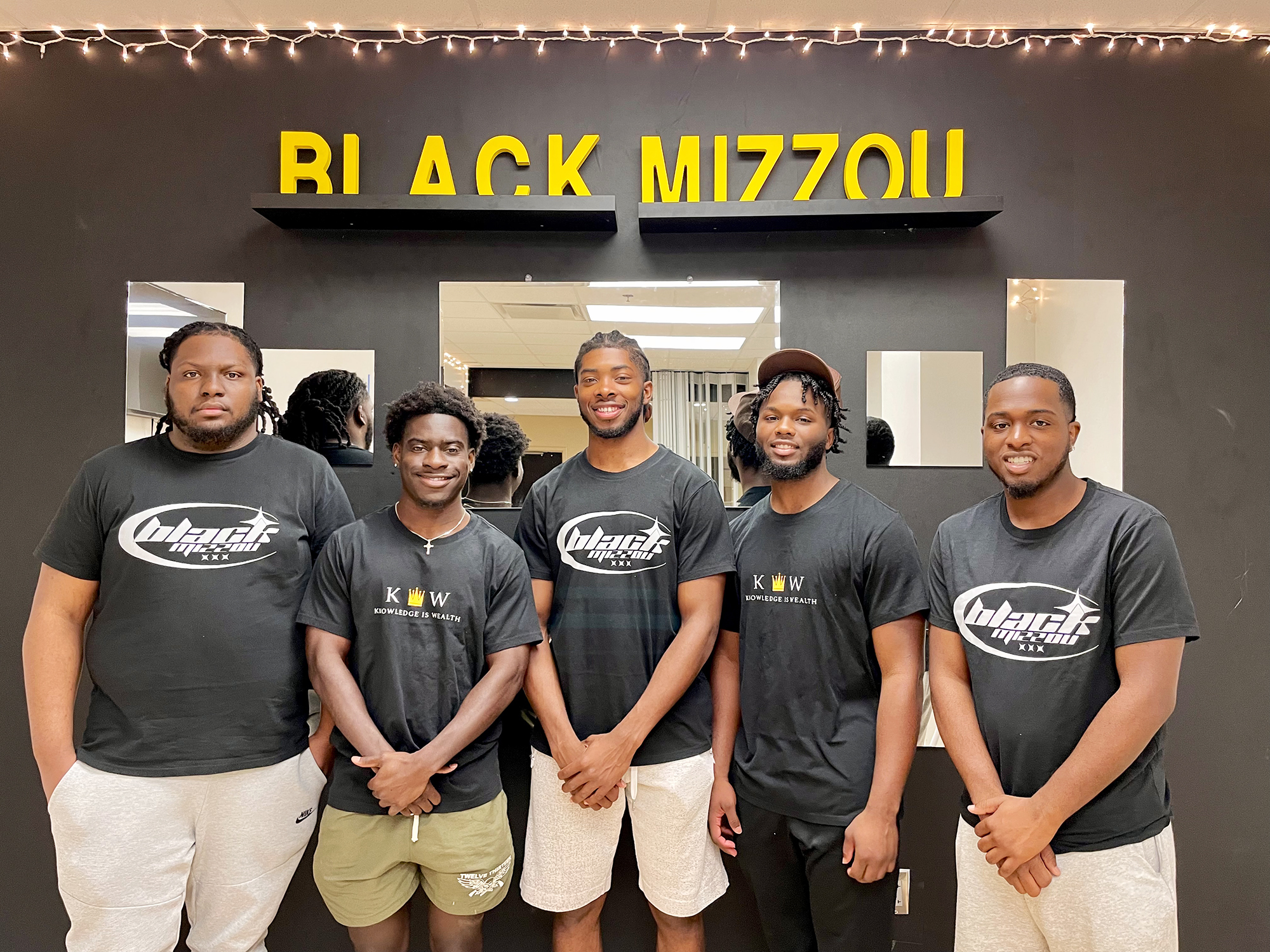 a group of five men stand in front of a "black mizzou" sign