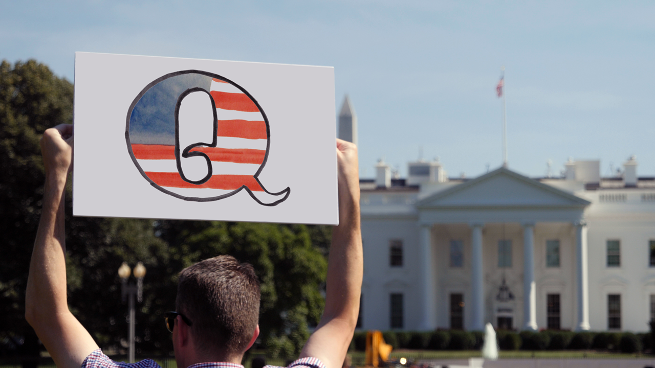 Picture of a person holding a sign with the letter Q in front of the White House source shutterstock