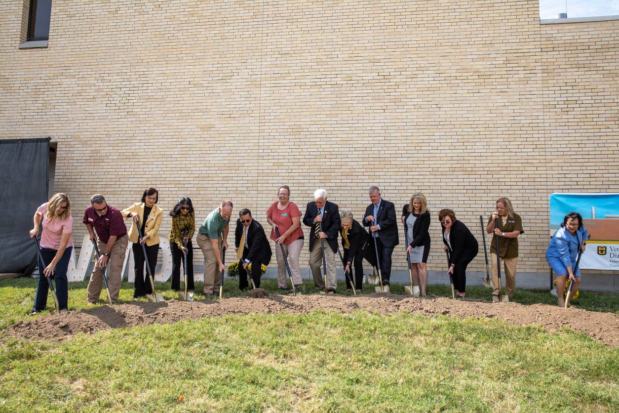This is a photo of attendees shoveling dirt from the ground.