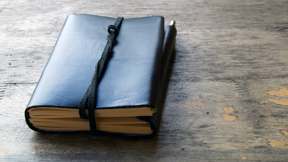 A leather-bound journal book sitting on a wood table source shutterstock