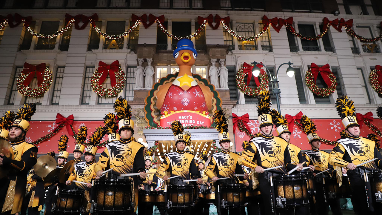 marching mizzou drummers in front of the macy's thanksgiving day parade sign