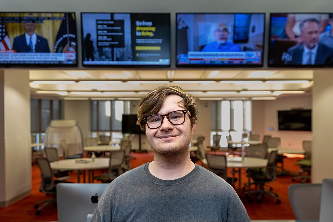 Brandon Ford poses in front of bank of TVs in the Reynolds Journalism Institute