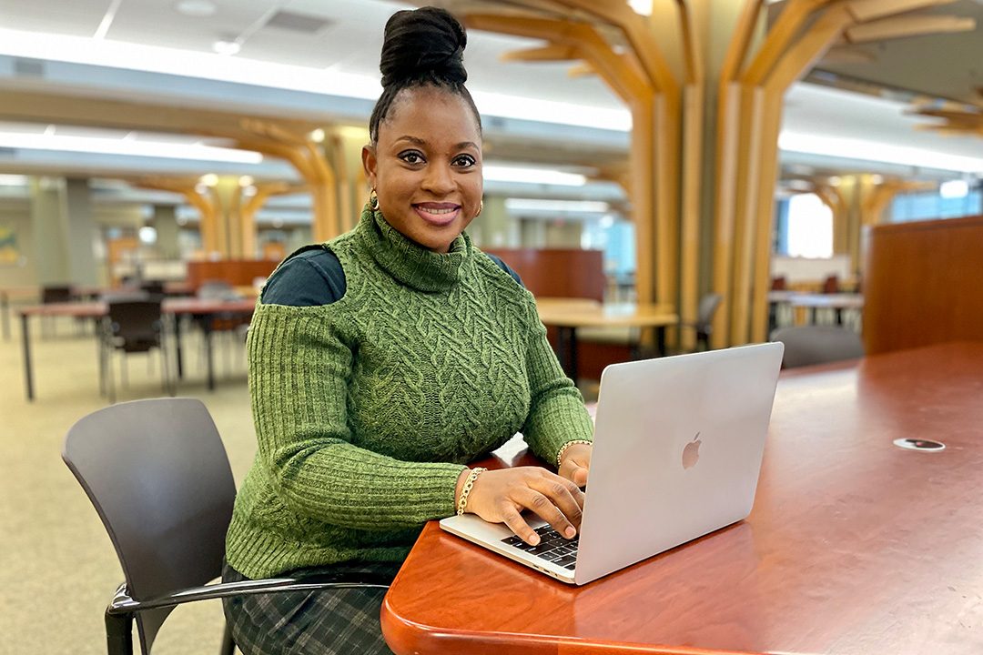 Jessica Osaze poses in front of laptop computer in MU's Ellis Library.