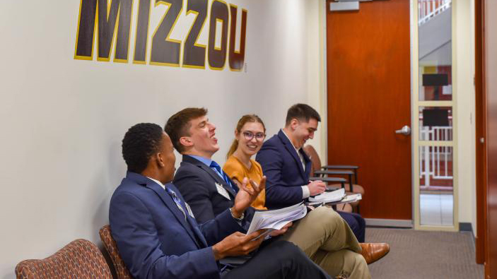 four students sit under a mizzou sign in a hallway