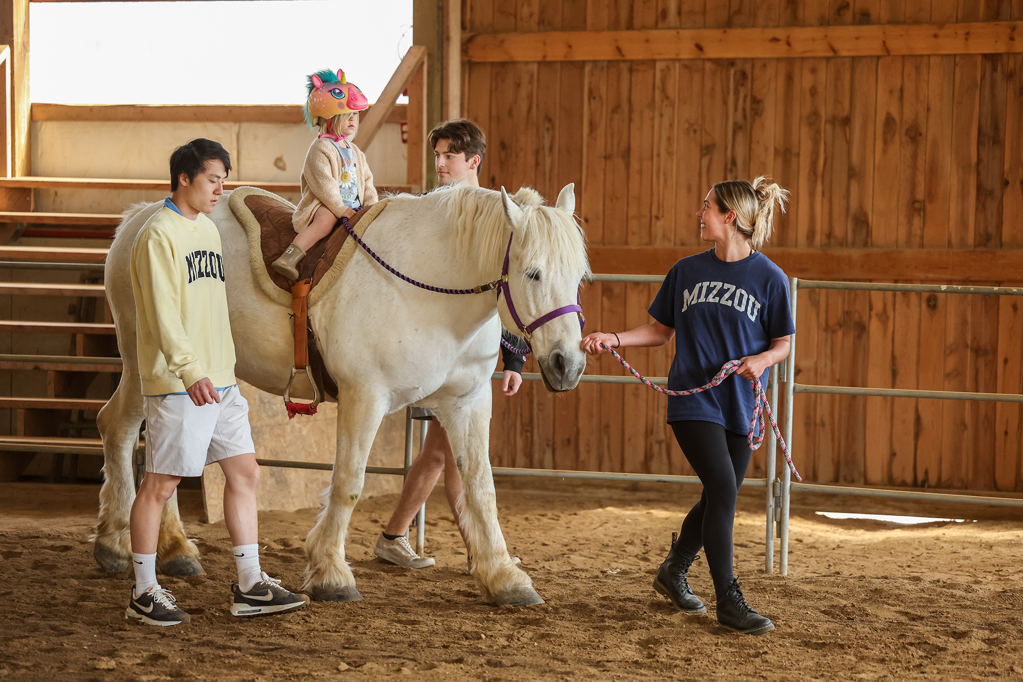 Small girl rides white horse while students wearing Mizzou shirts assist