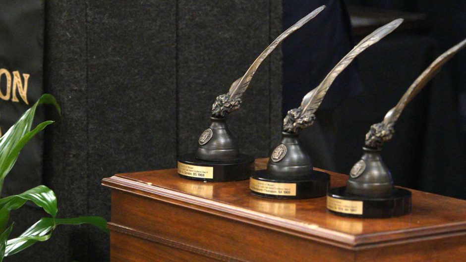 three golden quill statues on a table