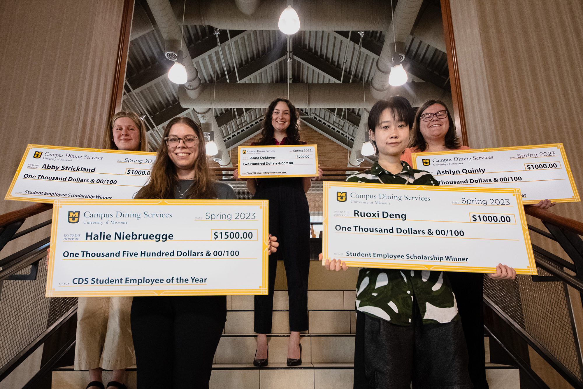 Five scholarship-recipient students hold oversized checks on stairs