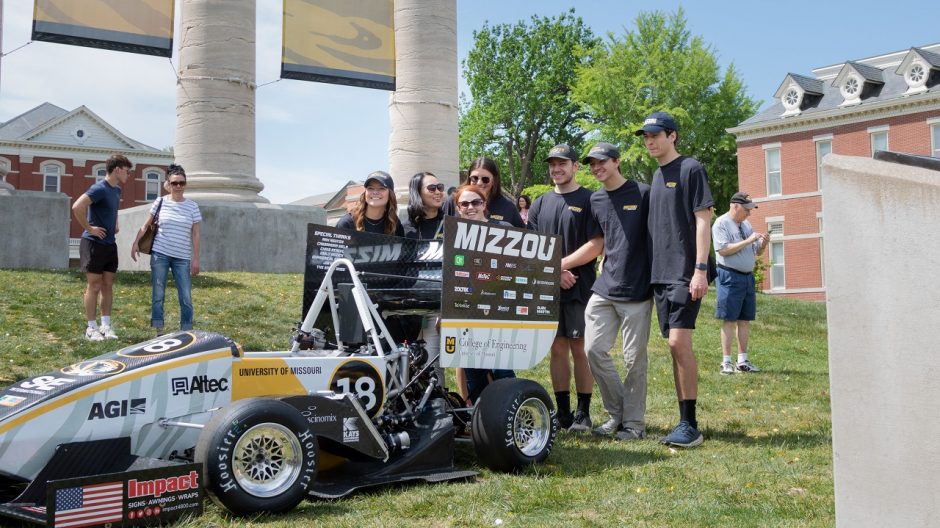 Formula SAE students stand next to their racecar.