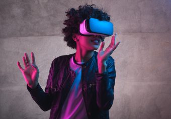 Person wearing a stand-alone VR headset in purple and blue light in front of a gray background