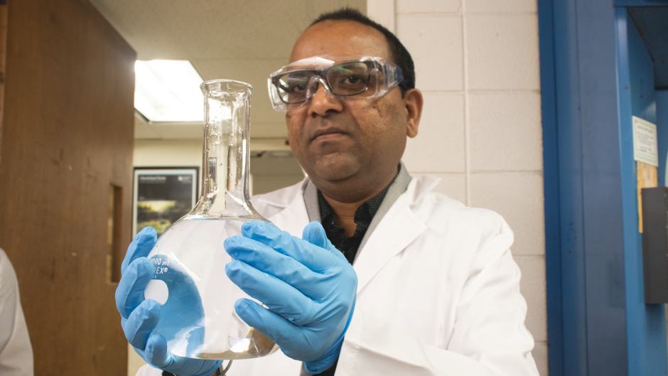 Photo of Sachin Handa in the lab holding a container of water