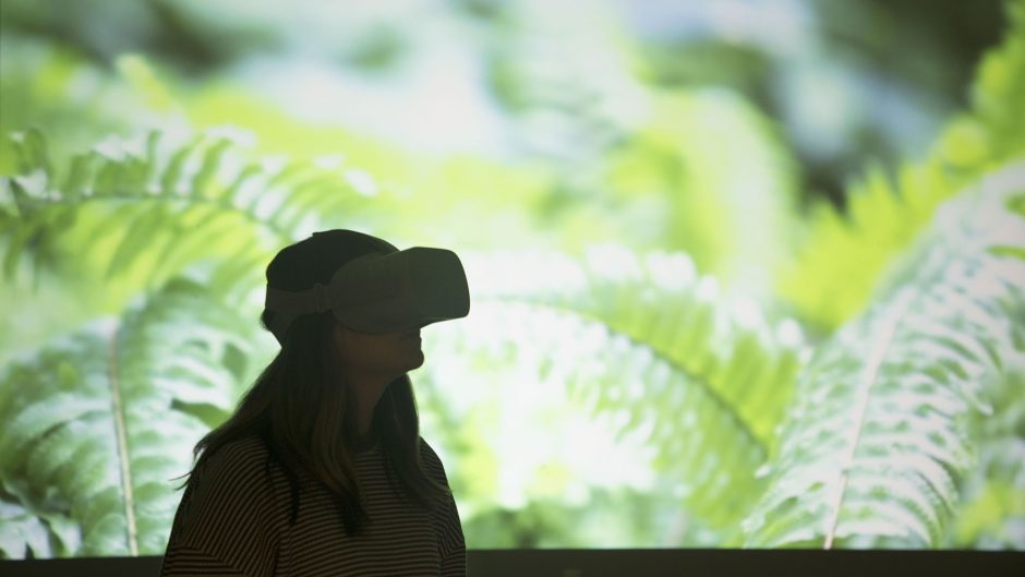 a girl wearing VR goggles with greenery on a screen behind her