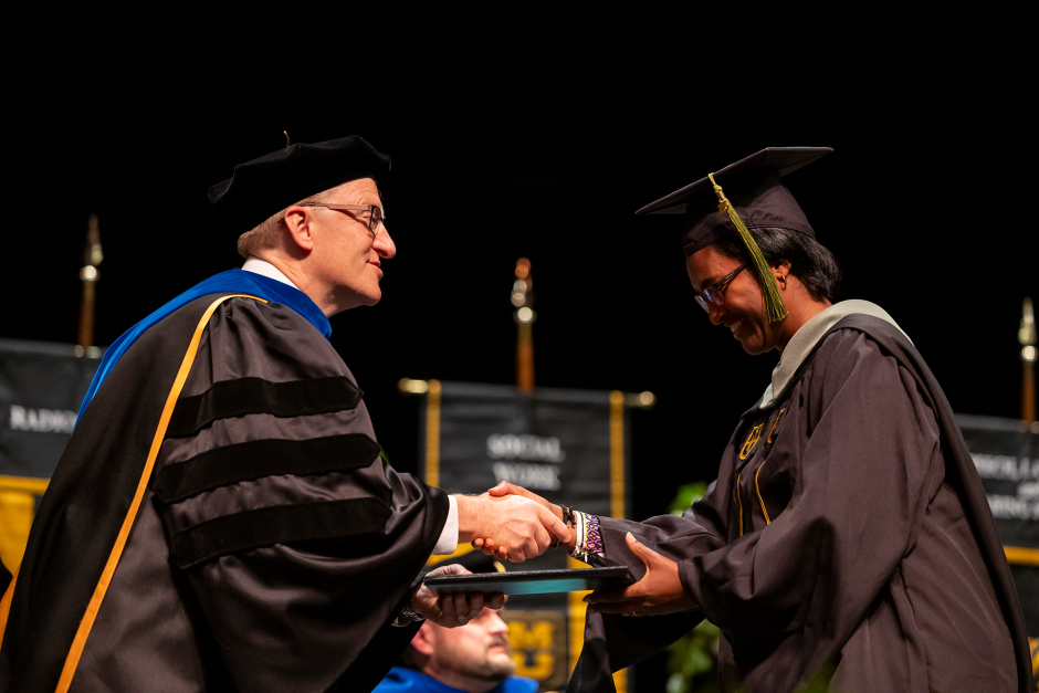 a graduate shaking hands while being handed a diploma