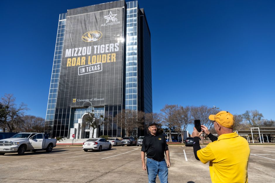 A man poses in front of the Mizzou Tigers Roar Louder sign on the Copeland building in Texas.