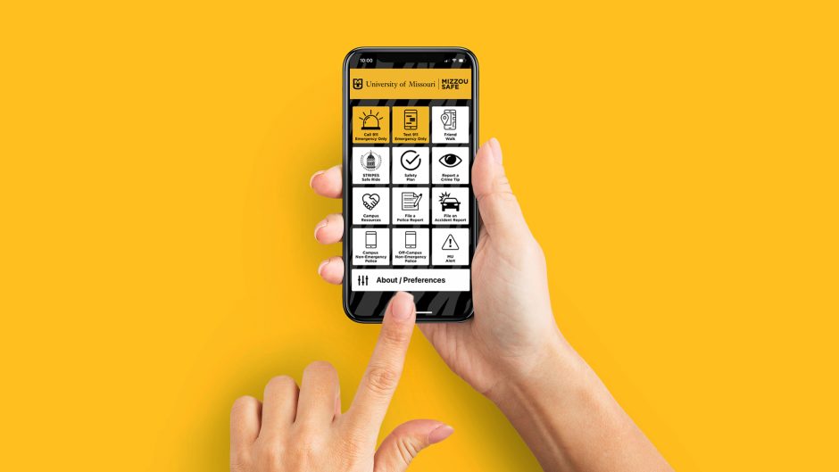 Mockup of female hands touching cell phone with Mizzou Safe app screen on gold background.