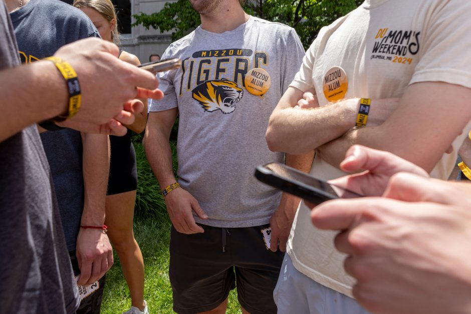 Students wear Mizzou alumni buttons as they look at their phones