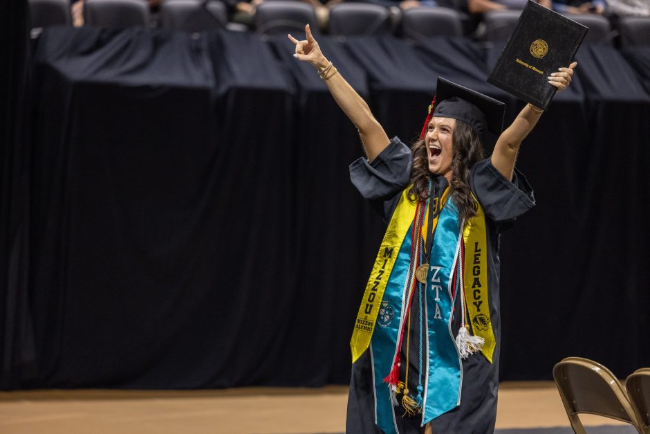 Student raises arms with degree
