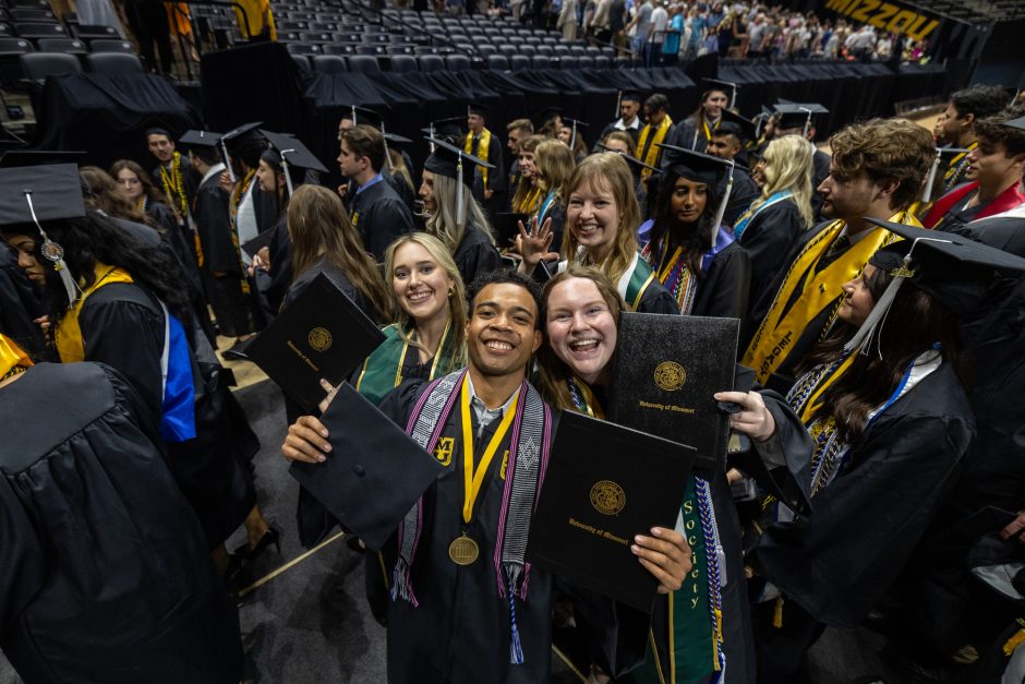 Graduates hold up degrees as they smile at camera 