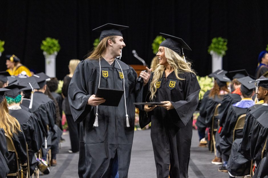 Two students walk with degrees