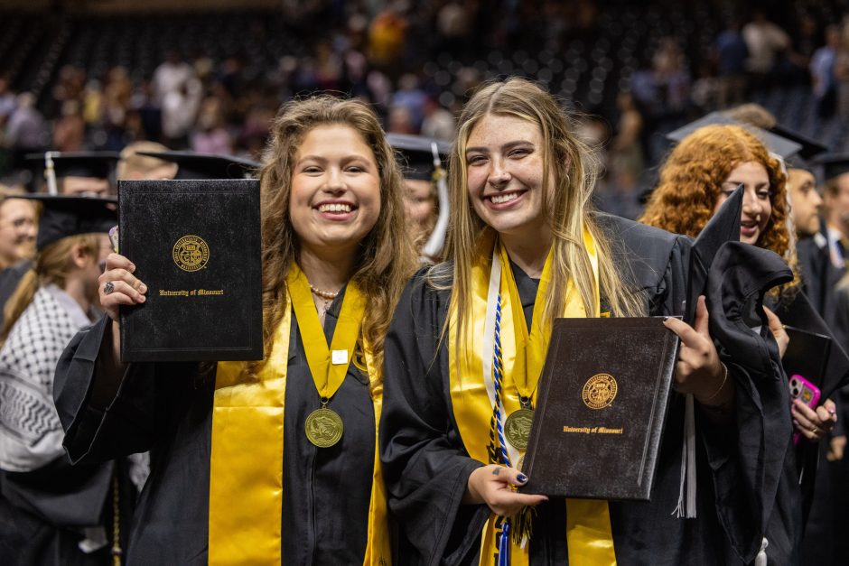 Two students hold up degrees