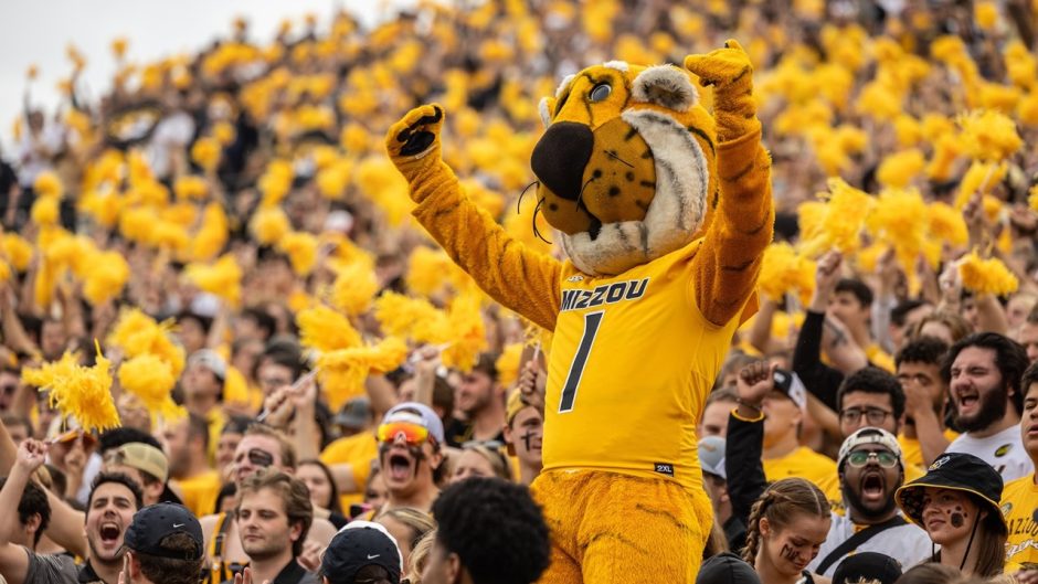 Truman the Tiger in a football jersey standing among students cheering in a football stadium